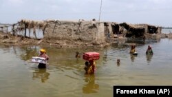 Women carry belongings salvaged from their flooded home after monsoon rains in Pakistan's Sindh Province. 