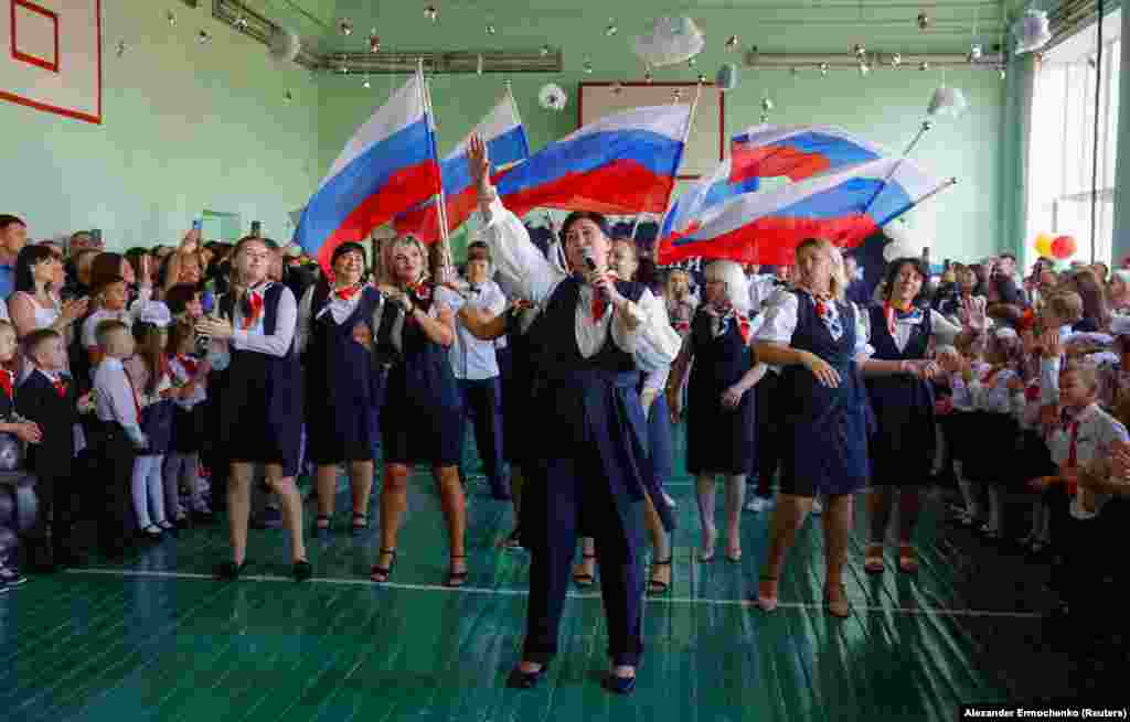 Children watch as people waving Russian flags welcome them to the start of the new school year at a lyceum in Ukraine's Russian-occupied Donetsk on September 2.
