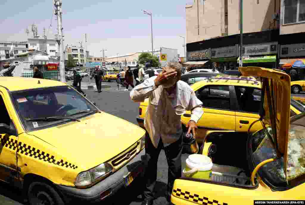 A man in Tehran splashes his face with water from the back of his taxi. 