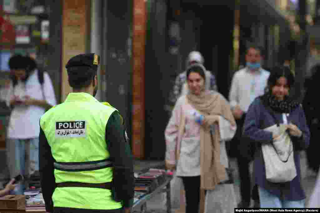 A policeman in Tehran as a woman (right) walks with her hair uncovered. Earlier this month, dozens of cafes and other businesses throughout Iran were shut down for purportedly allowing women to go uncovered. 