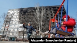 Дзеці гуляюць перад пашкоджаным будынкам у Марыюпалі, 23 сакавіка 2022 году