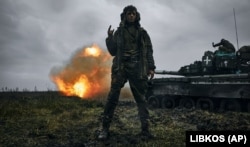 Украинский военный позирует для фото, пока его сослуживцы ведут огонь из трофейного танка Т-80 по позициям армии РФ в Донецкой области. 22 ноября 2022 года