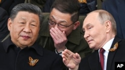Президент России Владимир Путин и лидер Китая Си Цзиньпин беседуют на трибуне во время военного парада в честь Дня Победы в Москве. 9 мая 2025 года