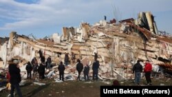  Люди смотрят на разрушения, пока спасатели ищут выживших в развалинах после землетрясения в Хатае, Турция, 7 февраля 2023 года.