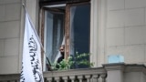 An official uses his smartphone next to the flag of the Islamic Emirate of Afghanistan at the balcony of the Afghan embassy in Moscow on July 4, 2025.