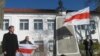 Юры Глебік побач з помнікам Кастуся Каліноўскага трымае бел-чырвона-белы сьцяг у руках
