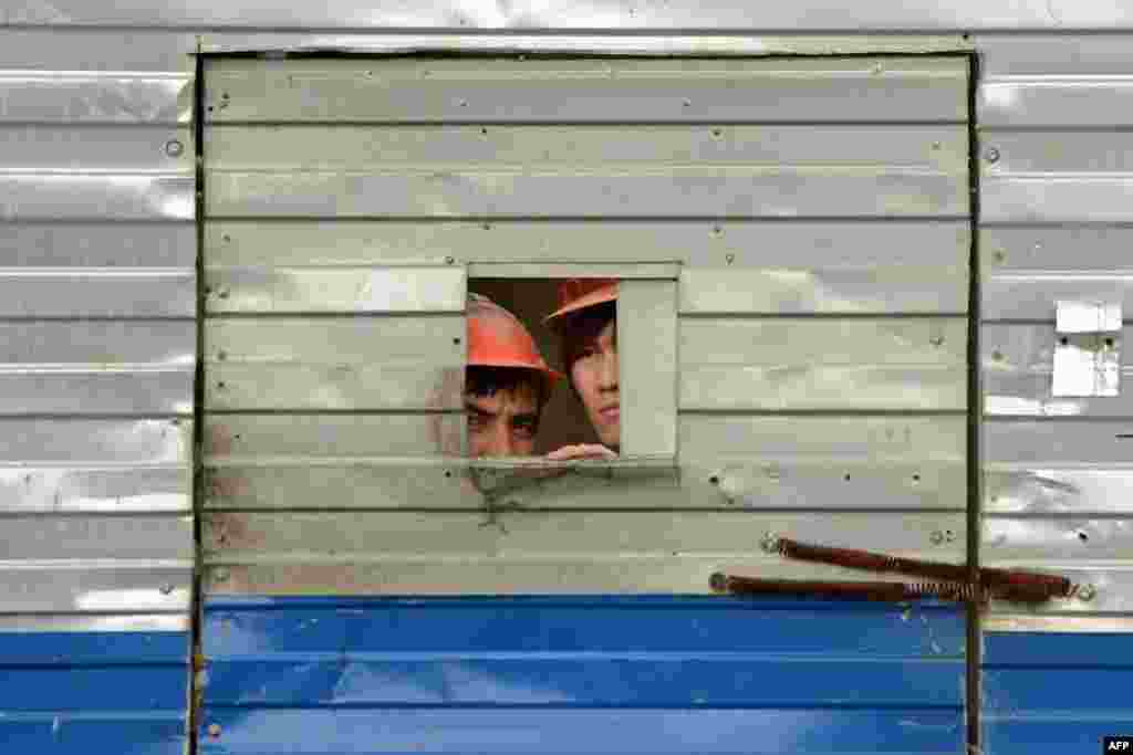 Migrant workers look through a door opening at a Moscow construction site to watch a Russian Orthodox religious procession in May 2013.