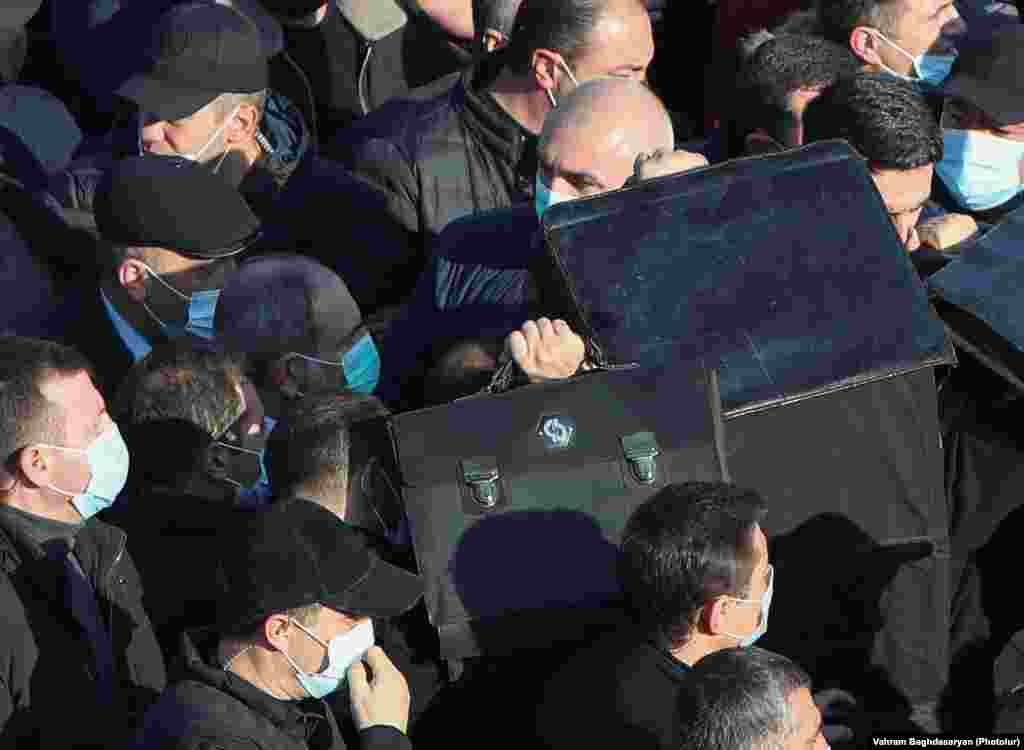 Bodyguards screen Armenian Prime Minister Nikol Pashinian with ballistic shields as he enters Yerablur cemetery on December 19. Pashinian faced anger from many in the grieving crowds who shouted, "Nikol, you traitor!" 