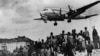 Un avion american de tic C-54 Skymaster în curs de aterizare la Baza militară aeriană Tempelhof de la Berlin, în timp ce berlinezii privesc cu speranță la 10 august 1948. Podul aerian a funcționat timp de 15 luni după ce sovieticii au blocat orașul. Circa 101 dintre participanții la operațiune au murit, între care 40 de britanici și 31 de americani, în cea mai mare parte a lor datorită unor accidente nelegate de zbor.