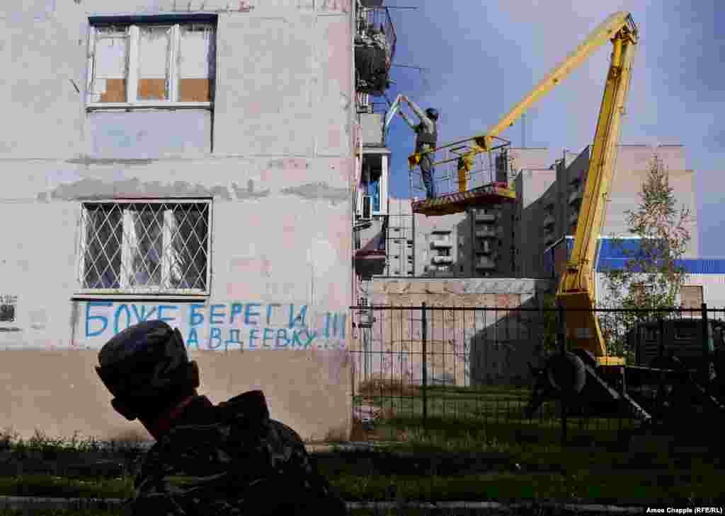 A Ukrainian soldier walks past as van Helten is lifted into position. The graffiti, in Russian, reads &quot;God Save Avdiyivka.&quot;&nbsp;