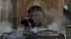 In old Avdiyivka village, a man named Borya cooks buckwheat porridge in a field kitchen beside a church damaged by a mortar overnight.