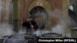 In old Avdiyivka village, a man named Borya cooks buckwheat porridge in a field kitchen beside a church damaged by a mortar overnight.