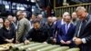 Ukrainian President Volodymyr Zelenskiy (signing a shell in the center of the picture) visits a munitions manufacturing plant with Ukrainian Ambassador to the United States Oksana Markarova in the background (far left). 
