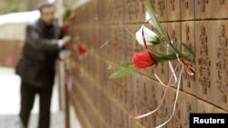 A man puts flowers into a wall with the names of slain Polish officers during a commemoration ceremony at a memorial complex in Katyn on April 10.