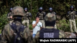 Член групы мігрантаў стаіць, спрабуючы пацьвердзіць жаданьне падаць заяву аб міжнароднай абароне ў Польшчы, у невялікай вёсцы Уснар Горны, недалёка ад мяжы зь Беларусьсю, 20 жніўня 2021 года