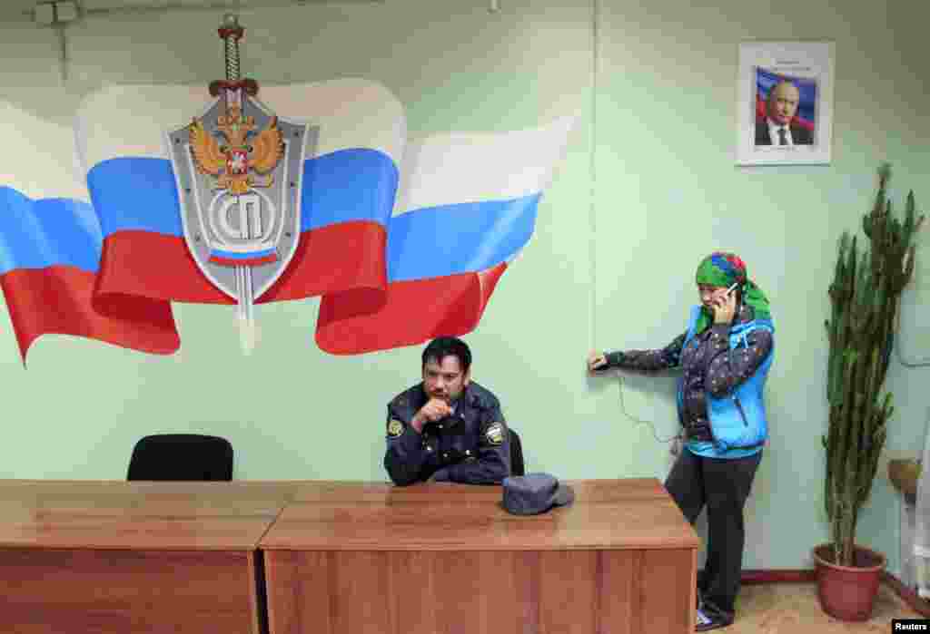 A police officer in Krasnoyarsk waits as a detained illegal migrant from Central Asia makes a telephone call before being deported in September 2013. 